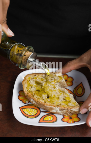 Drizzling olive oil on slice of bread Stock Photo