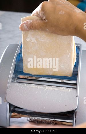 Rolling pasta dough through pasta machine to make pasta sheets Stock Photo