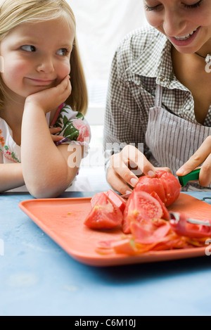 Teen girl showing young sister how to prepare tomatoes Stock Photo