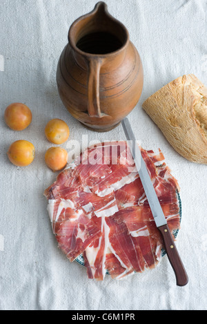 Plate of cut prosciutto with plum tomatoes and loaf of bread Stock Photo