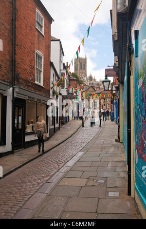 Lincoln city, Lincolnshire looking at the shops up Steep Hill cobbled road with tourists and shoppers cathedral at top Stock Photo