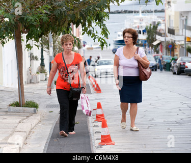 Two middle aged Greek women are walking up Leoforos Megalocharis avenue, in Tinos town, on the Greek Cyclade island of Tinos. Stock Photo
