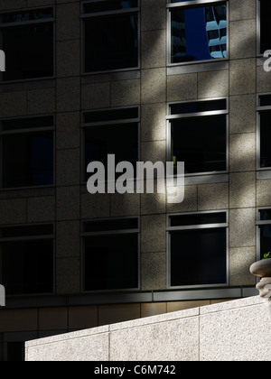 detail of empty office building plaza with stone ledge in bright sunshine seen dramatically against dark building in background Stock Photo