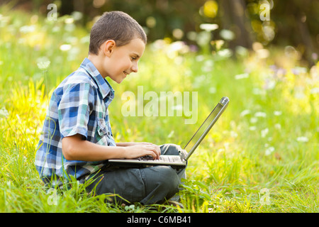 School boy using his laptop outdoor on a meadow Stock Photo