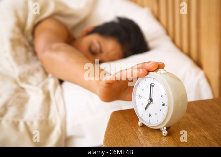 An Indian Asian woman wakes up and reaches to turn off a traditional alarm clock Stock Photo