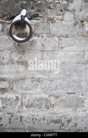 Ancient gray stone wall with cast iron ring covered in snow Stock Photo