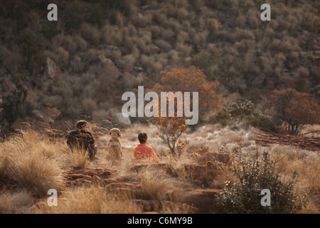 Rear view of a couple and their dog sitting on a hillside in dry vegetation Stock Photo