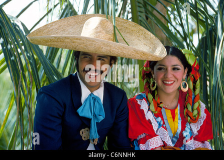 A traditional Mexican folkloric dance couple in their colorful costumes relax in the shade of palms between performances in Puerto Vallarta, Mexico. Stock Photo