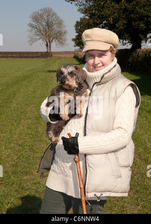 A young woman holding a Miniature Wirehaired Dachshund dog in the countryside
