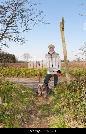 A young woman walking a Dog on a lead along footpaths in the countryside Stock Photo