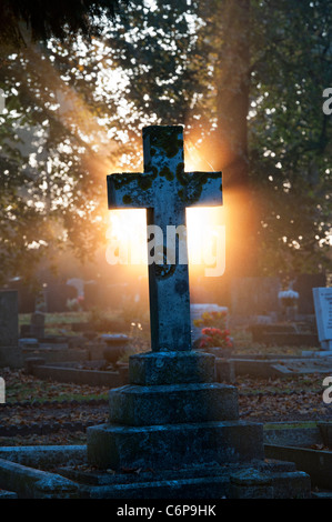 Cemetery Cross headstones lit up in the early morning sunlight through mist. Kings Sutton, Northamptonshire, England Stock Photo
