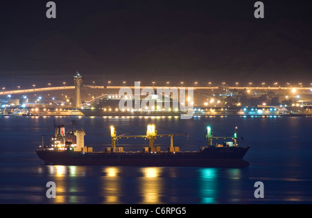 An anchored dry bulk freighter at night. In the background: MS 'The World' moored at the port of Aqaba, Jordan. Stock Photo