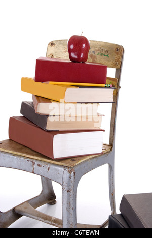 A vintage child's school chair holding a stack of books with a red apple and pencil perched on top against a white background. Stock Photo