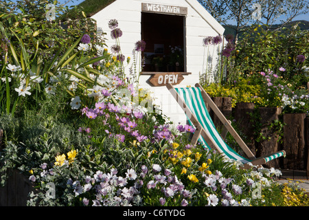 Painted shed and flowers with deckchair seating - colourful raised bed beds flowerbed flower borders border UK Stock Photo