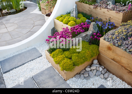 A modern garden with circle circular round stone paved paving patio and raised beds made from old wooden wood sleepers alpine plants in containers UK Stock Photo