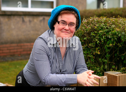 Susan Boyle in high spirits while happily chatting to photographers outside her house, wearing a blue hat and striped shirt. Stock Photo