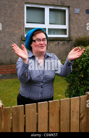 Susan Boyle in high spirits while happily chatting to photographers outside her house, wearing a blue hat and striped shirt. Stock Photo