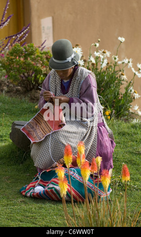 An Indian woman, dressed in traditional style and wearing the hat seen everywhere in Bolivia, sits in her garden to crochet. Stock Photo