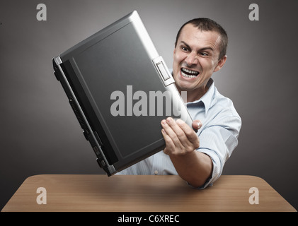 Extremely angry businessman smashing his laptop on the desk Stock Photo
