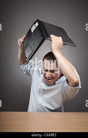 Extremely angry businessman smashing his laptop on the desk Stock Photo