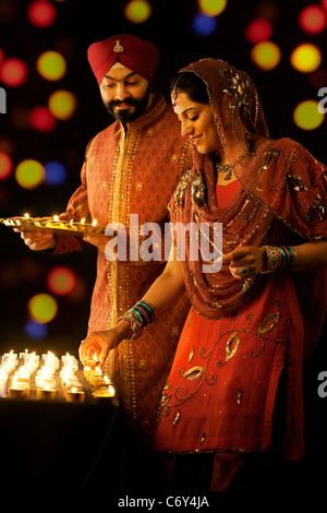 Sikh man holding a tray of diyas while the woman places them on a table Stock Photo