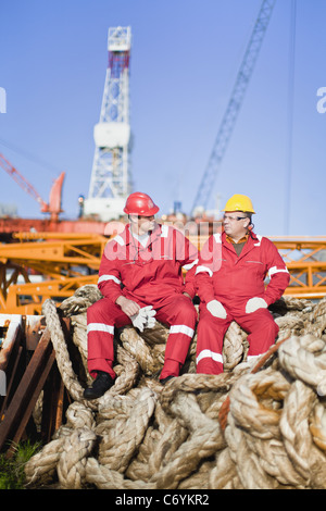Workers sitting on rope on oil rig Stock Photo