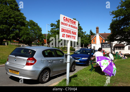 New BMW next to sign warning drivers they park by the cricket ground at their own risk while a match is in progress, Southborough Common, Kent, UK Stock Photo