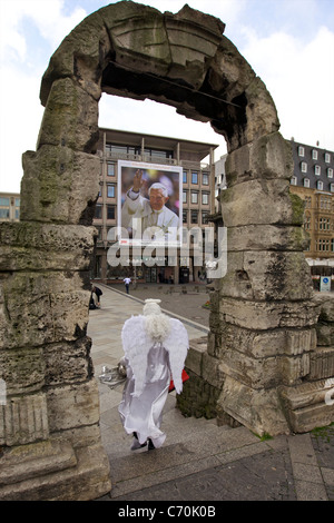 Performing Artist passing through Roman portal in Cologne. Huge Poster of Pope Benedict in the background, Germany Stock Photo