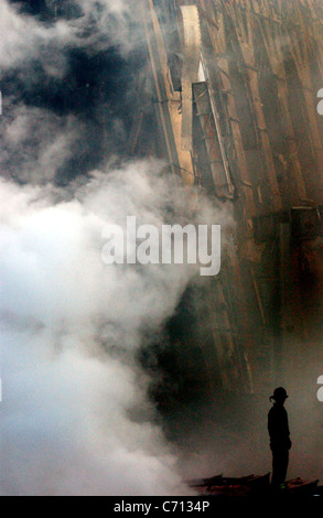 A solitary Firefighter stands watching as smoke rises from the rubble and debris of the World Trade Centers in New York City in the area know as Ground Zero, after the 9/11 terrorists attacks. Stock Photo