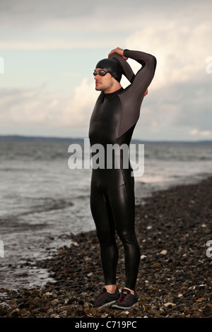 A triathlete stands and stretches to get ready for his swim. Stock Photo