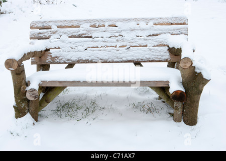 Rustic Garden bench made from old logs covered in snow winter Stock Photo