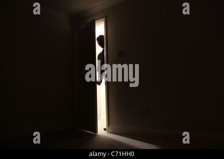 Silhouette of a male standing outside a dark room looking in. Stock Photo