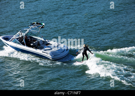 A happy athletic woman wake surfs behind a wakeboard boat in Idaho. Stock Photo