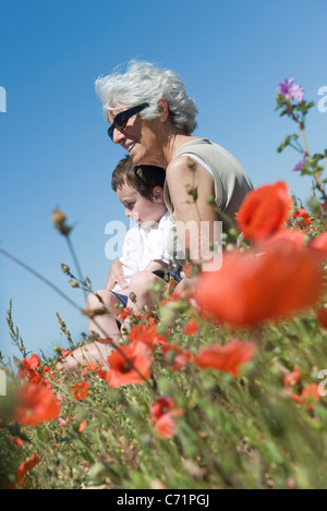 Grandmother and young grandson sitting together in field of poppies