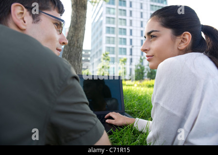 Man and woman looking at each other while using laptop computer outdoors Stock Photo