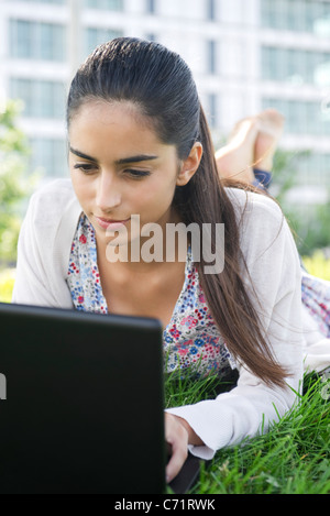 Young woman lying on stomach on grass using laptop Stock Photo