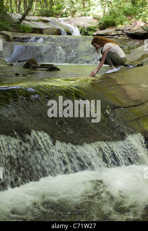 Woman crouching beside cascading stream, dipping hands in water Stock Photo