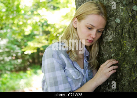 Young woman leaning against tree, looking sad