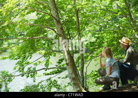 Couple crouching by lake looking at view Stock Photo
