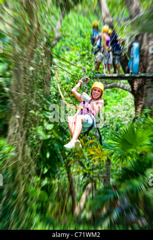 Woman flies through tropical jungle canopy on zipline Stock Photo