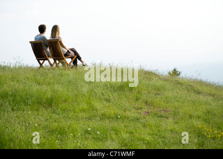 Couple sitting on chairs on top of hill looking at view Stock Photo