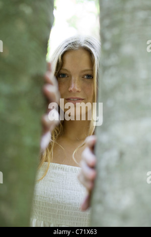 Young woman peering out from behind tree trunks Stock Photo