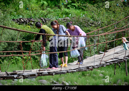 Three women are very nervous of crossing a primitive hanging bridge. Sichuan, China. Stock Photo