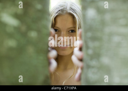 Young woman peering out from behind tree trunks Stock Photo