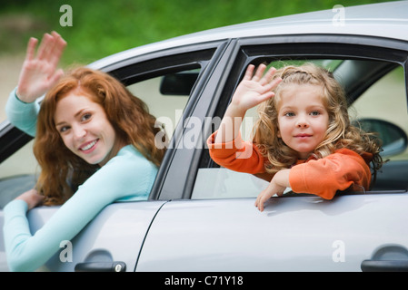 Mother and young daughter leaning out of car windows, waving Stock Photo