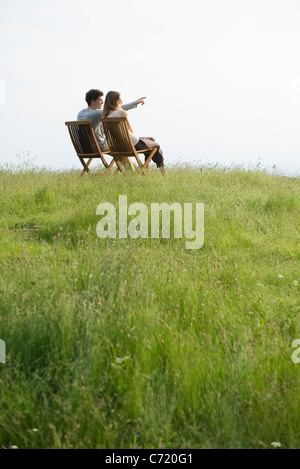 Couple sitting on chairs on top of hill looking at view, man pointing toward distance Stock Photo
