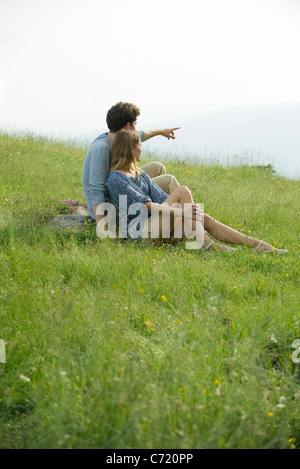 Couple sitting on meadow, man pointing toward distance Stock Photo