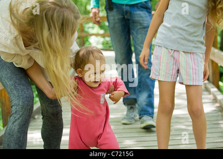 Baby girl learning to walk outdoors with family Stock Photo