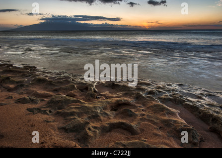 A beautiful sunset over a Maui beach with the waves lapping over the coral on the beach Stock Photo