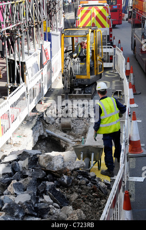 Looking down on mini digger excavator & worker in narrow space for road works red double decker squeeze past Regent Street West End London England UK Stock Photo